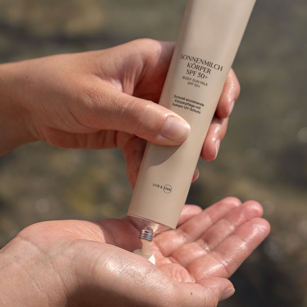 Person drückt Sonnenmilch aus Tube in Hand. Tube mit Aufschrift: SONNENMILCH KÖRPER SPF 50+.