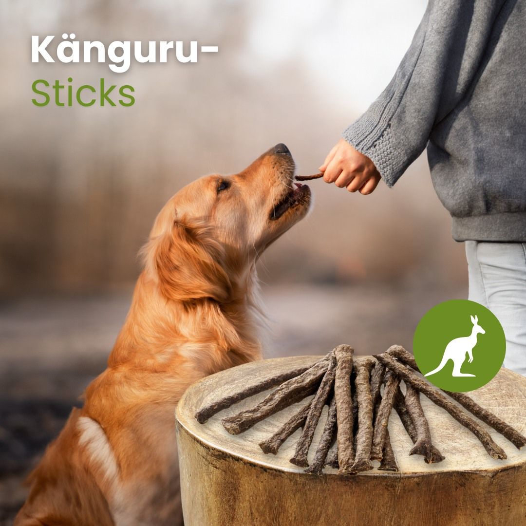 Hundefutter: Känguru-Sticks, 12-18 cm lang, auf einem Holzstamm gestapelt.