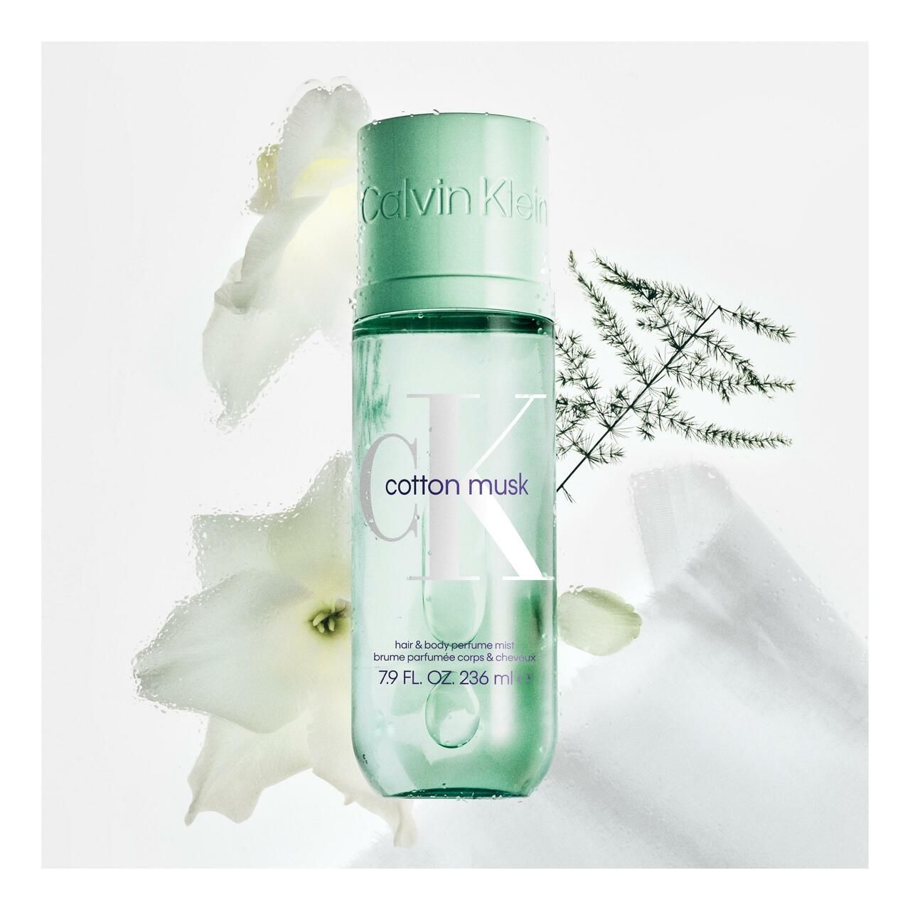 Grüne Flasche mit Sprühkopf. Aufschrift Calvin Klein, cotton musk, hair & body perfume mist. Mit weißen Blüten und Zweigen.