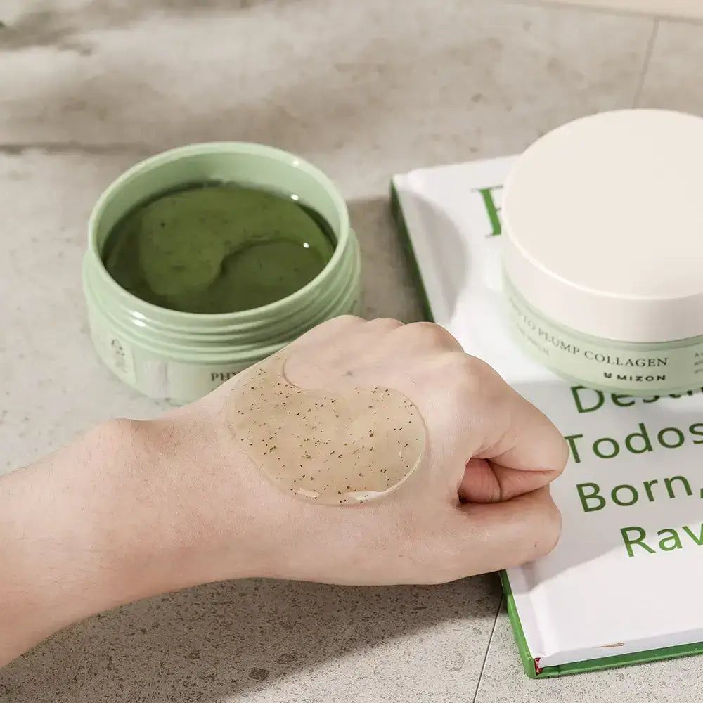 Offene Dose mit Augen-Gel-Pads. Gel auf Hand. Aufschrift: Phyto Plump Collagen Eye Gel Patch. Marke: Mizon. Buch im Hintergrund.