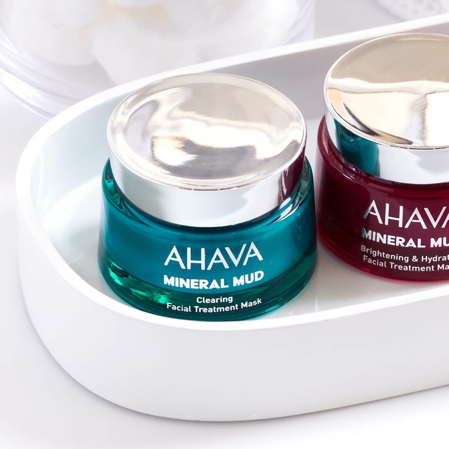 Ahava Mineral Mud Masken in weißer Schale. Türkis und rotbraune Gläser mit silbernen Deckeln. Produktnamen sichtbar.