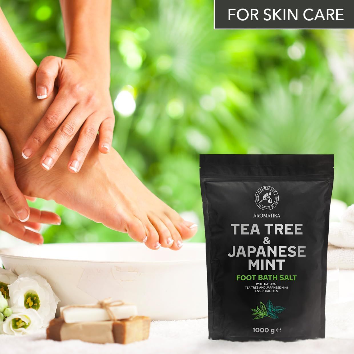 Fuß in Wasser mit Tea Tree & Japanische Minze Fußbadesalz. Schwarzer Beutel mit Aufschrift: Tea Tree & Japanische Minze. Marke: AROMATIKA. 1000 g.
