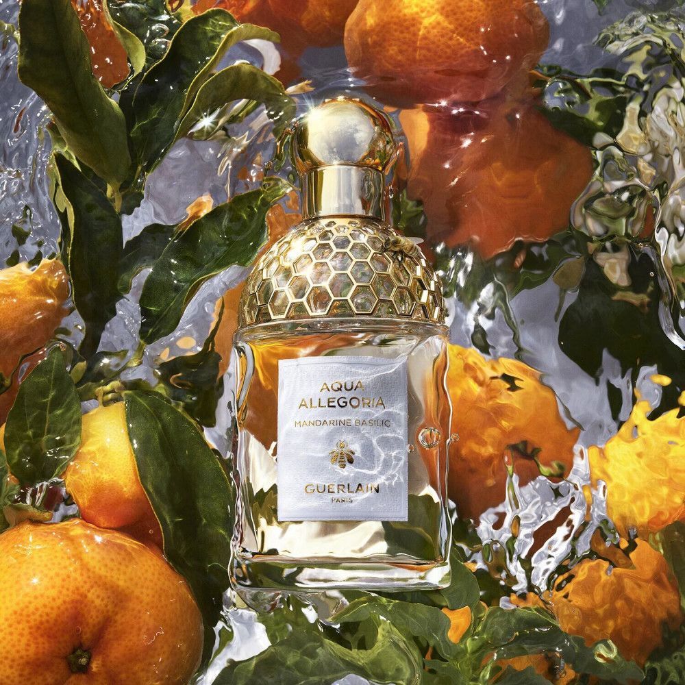 Parfümflakon in Wasser mit Mandarinen und Blättern. Aufschrift: Aqua Allegoria Mandarine Basilic, Guerlain.