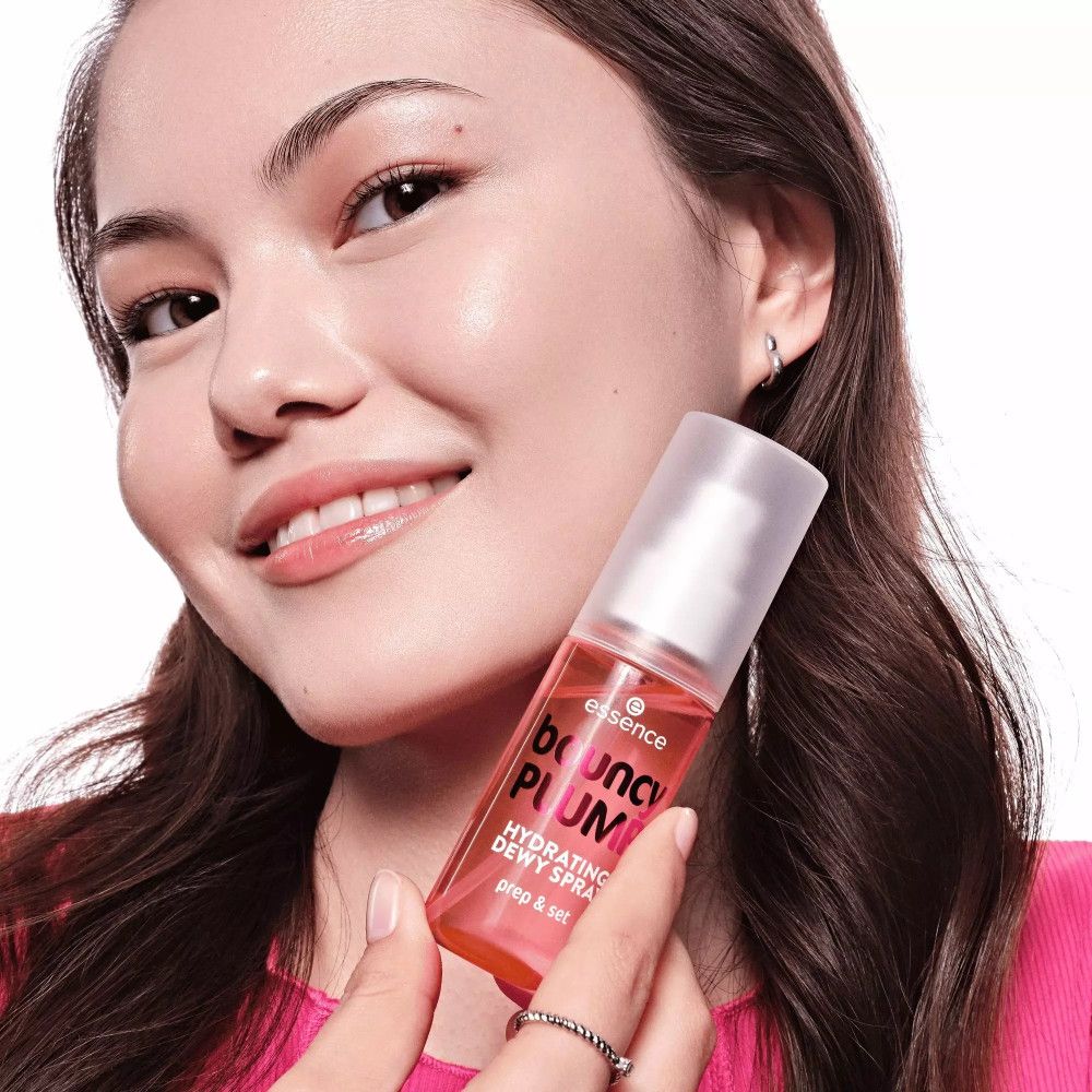 Frau hält rosa Flasche mit weißem Sprühkopf. Aufschrift: bouncy PLUMP, Hydrating Dewy Spray, prep & set. Marke: essence.
