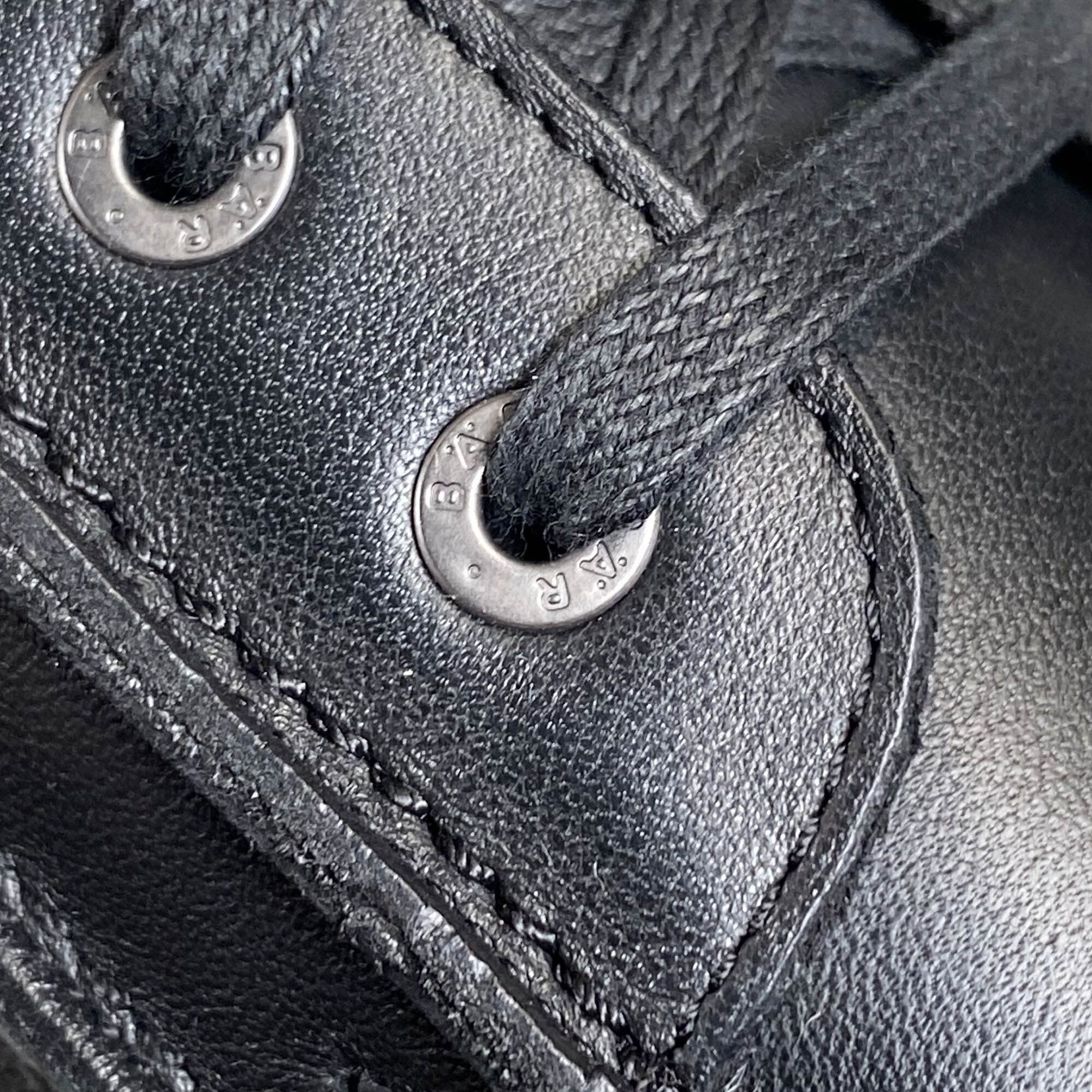 Nahaufnahme von Ösen mit Logo. Schwarzes Leder. Metallösen mit Prägung.
