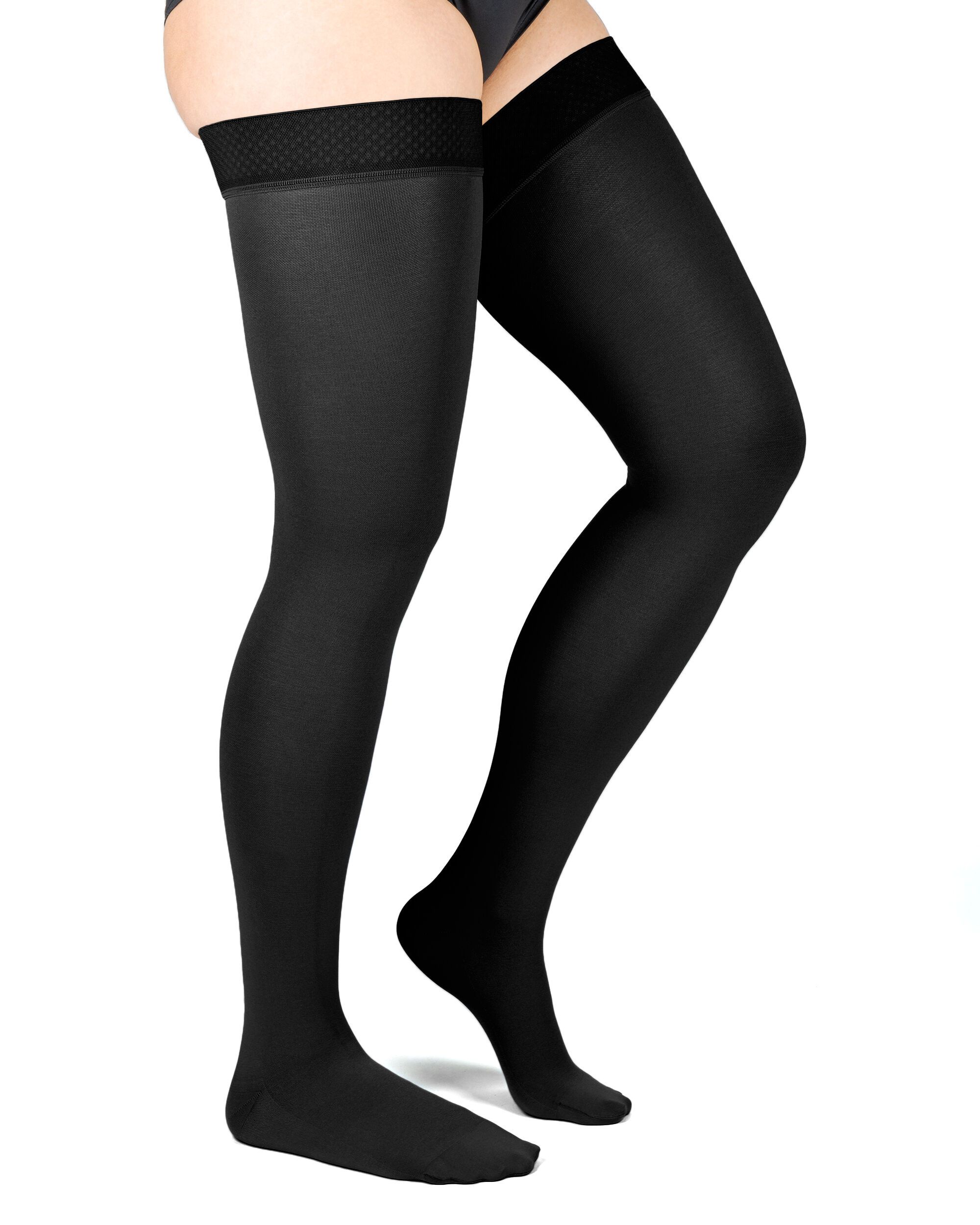 Schwarze Kompressions-Schenkelstrümpfe. Oberschenkelhoch, mit strukturiertem Abschlussband. Blick von der Seite, auf einem Bein getragen.