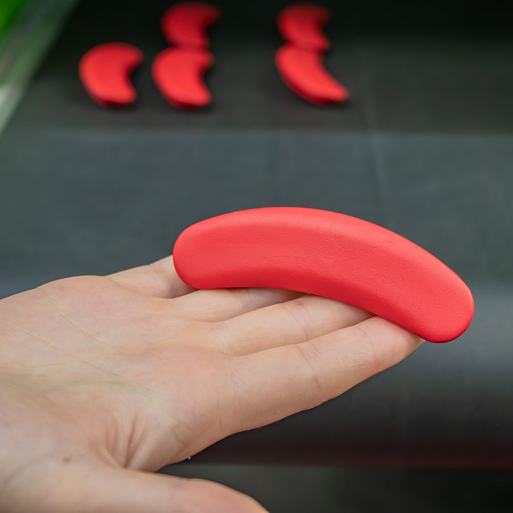 Roter, gebogener Griff in einer Hand. Mehrere rote Griffe im Hintergrund.
