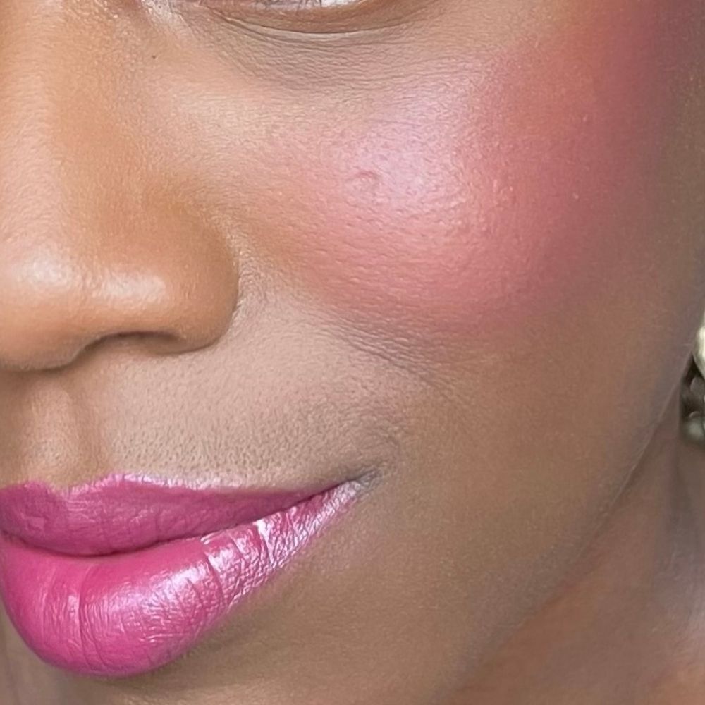 Nahaufnahme eines Gesichts mit rosa Rouge auf den Wangen und Lippenstift auf den Lippen. Dunkle Haut.