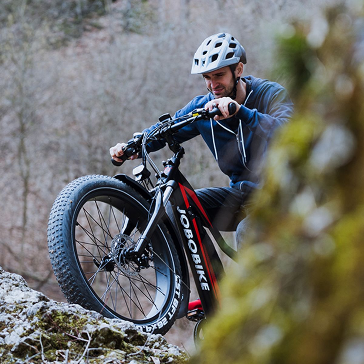 Person auf einem JOBOBIKE Robin E-Bike. Fährt auf einem steinigen Weg. Helm und Natur im Hintergrund.