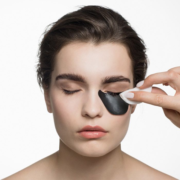 Person mit Augenpads. Eine Hand hält einen Wattepad. Die Person hat die Augen geschlossen.