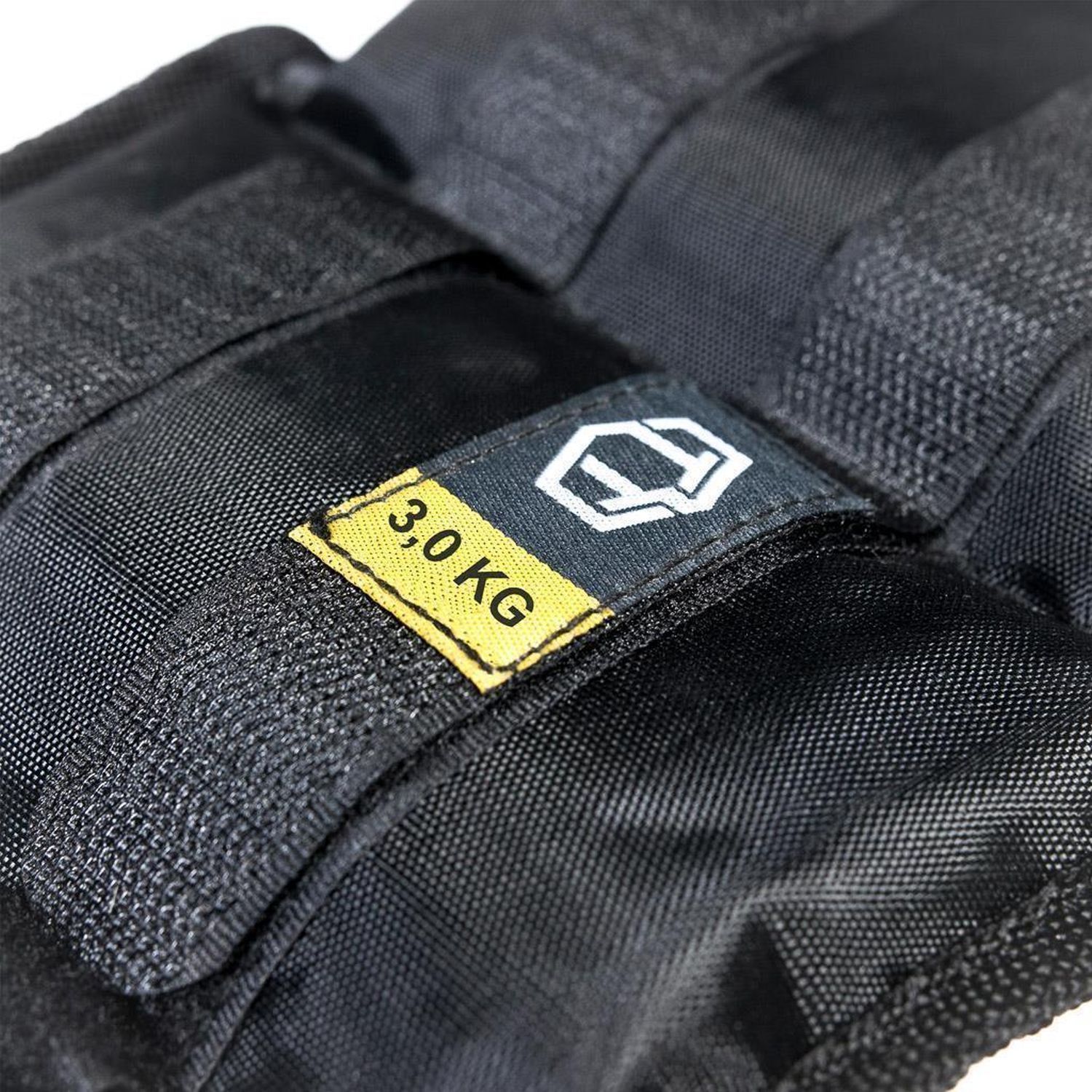 Schwarze Gewichtsmanschette mit gelbem Etikett, Aufschrift "3,0 KG". Logo auf dem Etikett. Schwarzes Textilmaterial.