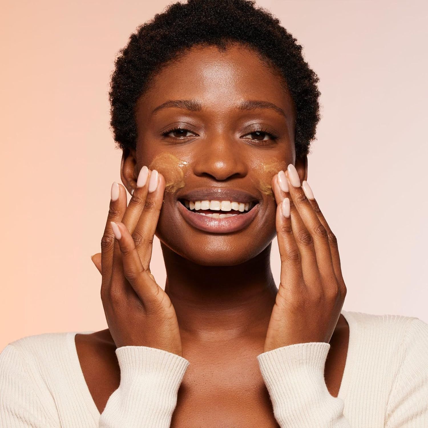 Frau trägt Produkt auf Gesicht auf. Gelbliche Substanz auf Haut. Lächelt.