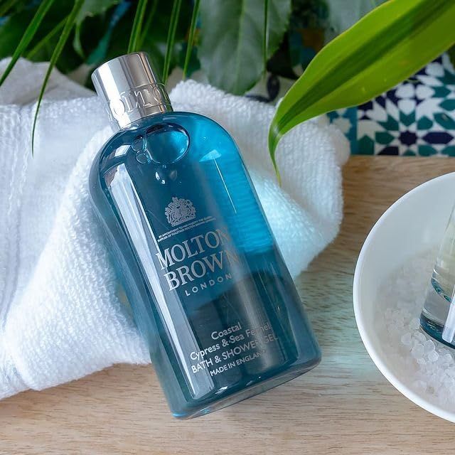 Molton Brown Duschgel auf einem Handtuch. Flasche mit silbernem Deckel. Auf einem Tisch mit Eiswürfeln.