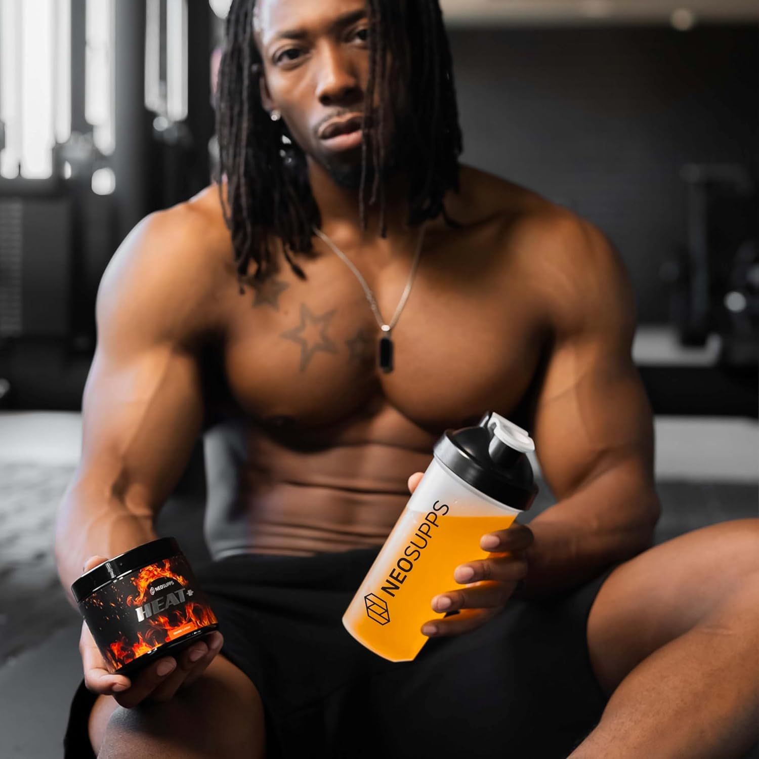 Mann hält Dose "HEAT+" und Shaker mit "NEOSUPPS"-Logo. Beide Produkte sind sichtbar. Mann sitzt.