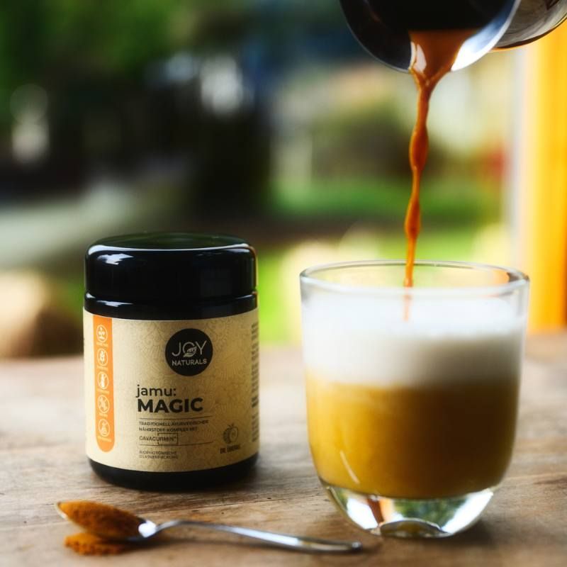 Bicchiere con bevanda, accanto un barattolo di JOY NATURALS jamu: MAGIC. Cucchiaio con polvere.