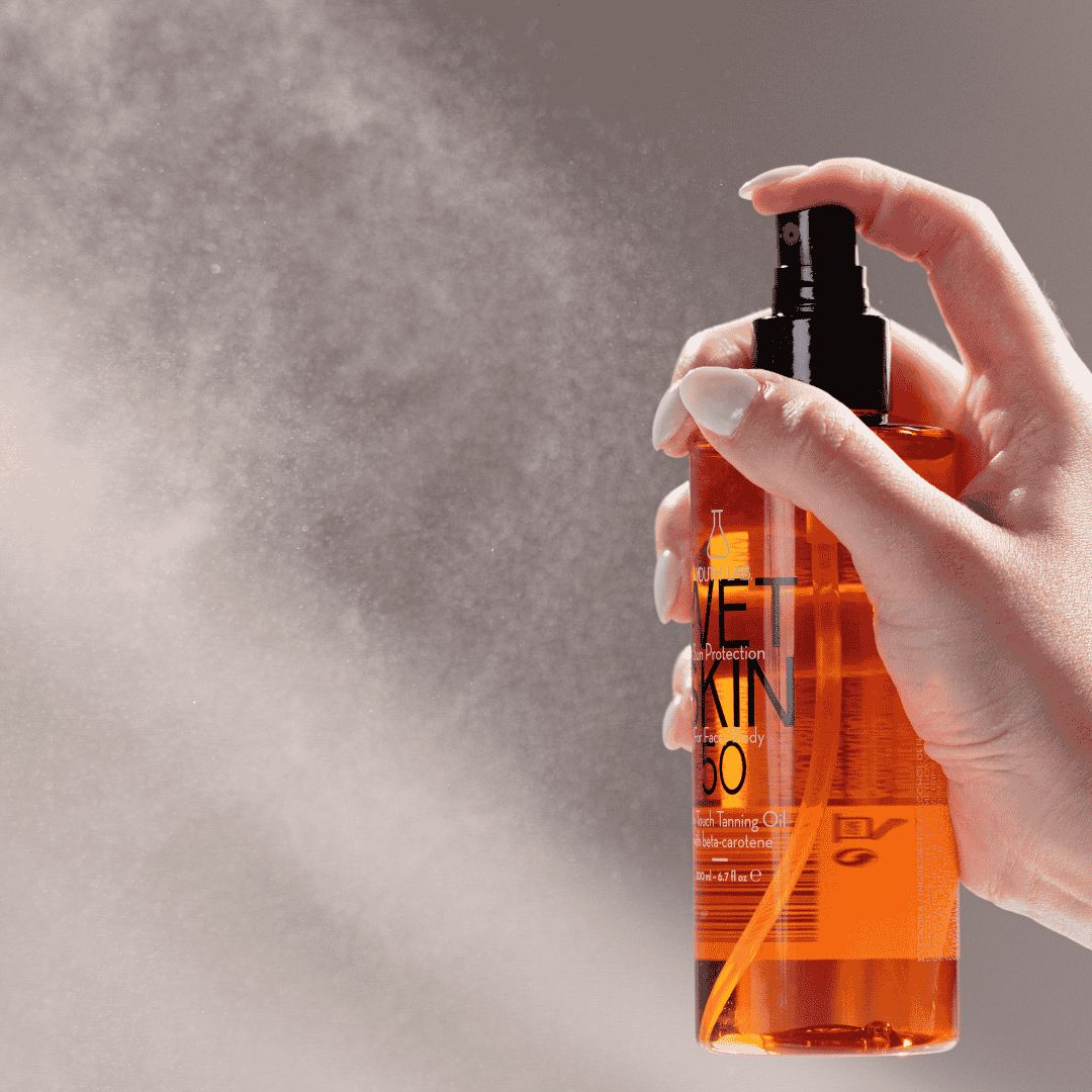 Hand sprüht Flüssigkeit aus einer orangefarbenen Flasche. Aufschrift: WET SKIN SPF 50. Schwarzer Sprühkopf.