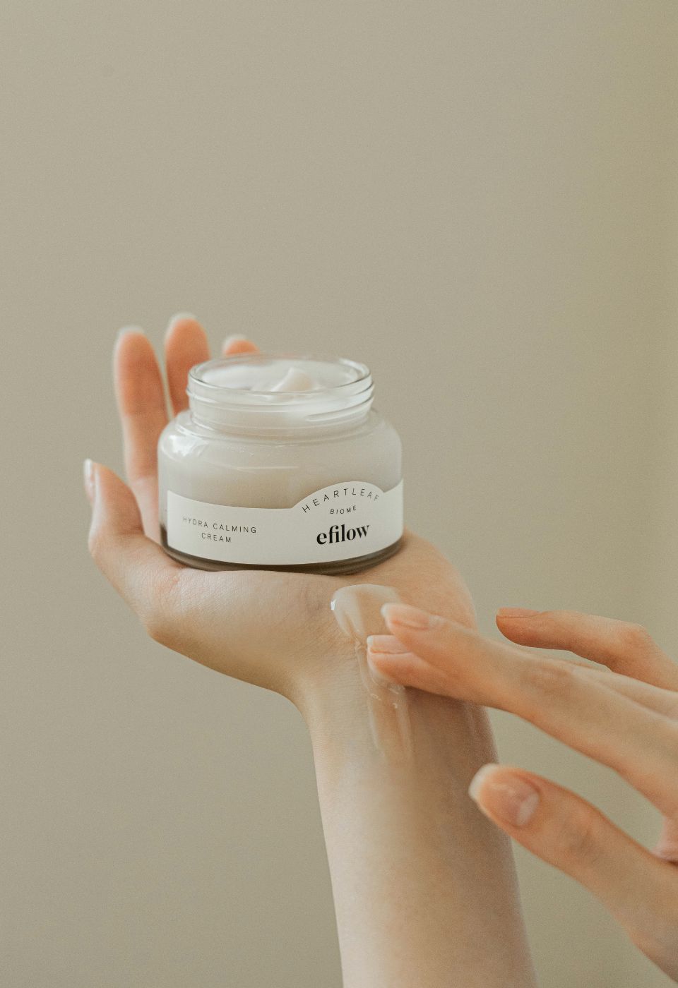Hände halten ein offenes Creme-Glas. Aufschrift: Heartleaf Biome, efilow, Hydra Calming Cream. Creme wird aufgetragen.