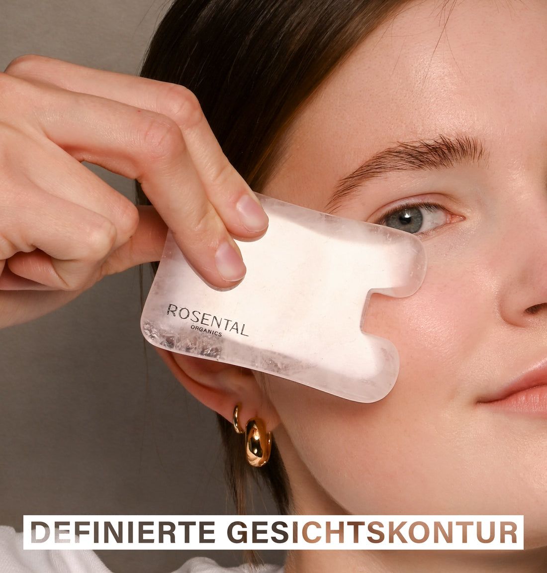 Person hält Rosental Organics Gua Sha aus Rosenquarz an der Wange. Text: Definierte Gesichtskontur.
