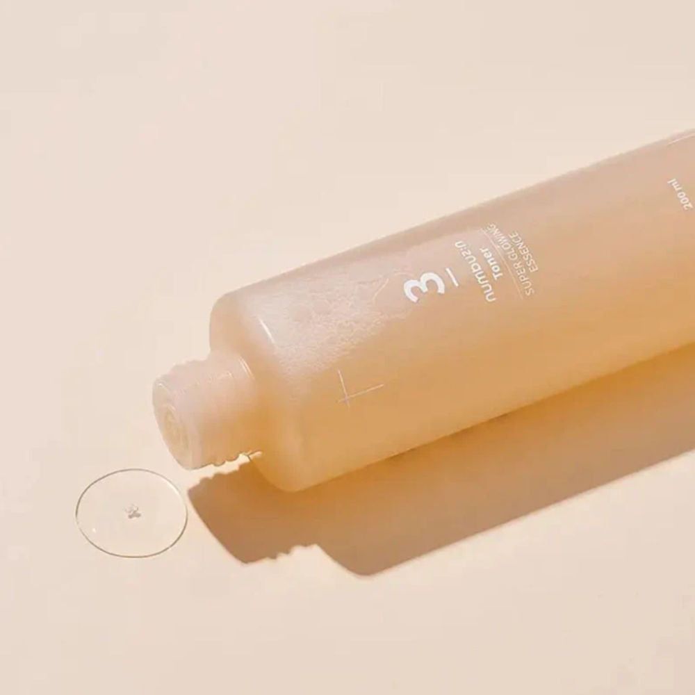 Flasche liegt, Flüssigkeit tropft heraus. Aufschrift: 3, Toner, Super Glowing Essence. Klare Flüssigkeit auf Oberfläche.