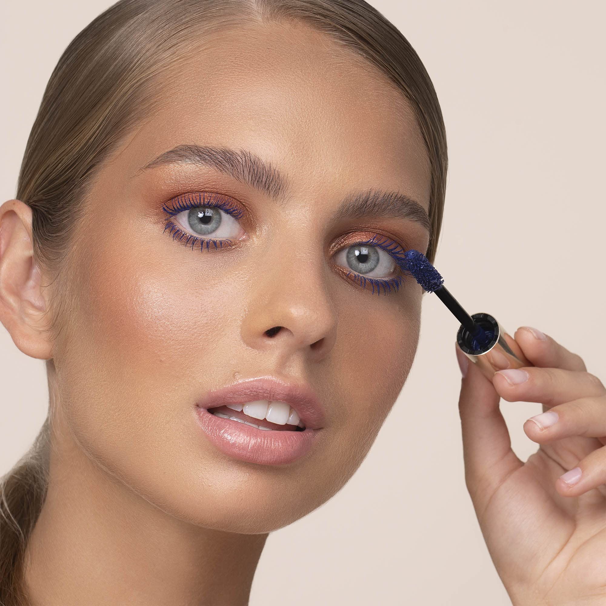 Frau trägt blauen Mascara auf. Goldene Mascarahülse sichtbar. Marke: BY TERRY.