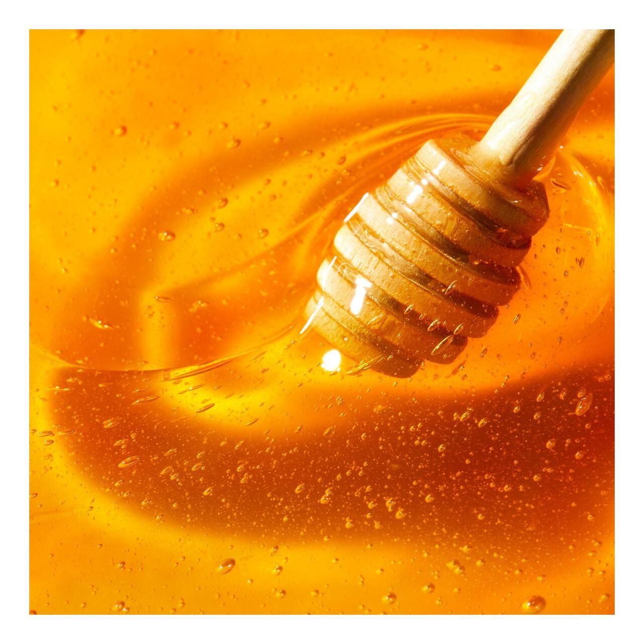 Honig mit Honiglöffel. Goldgelbe Farbe, glänzende Oberfläche.