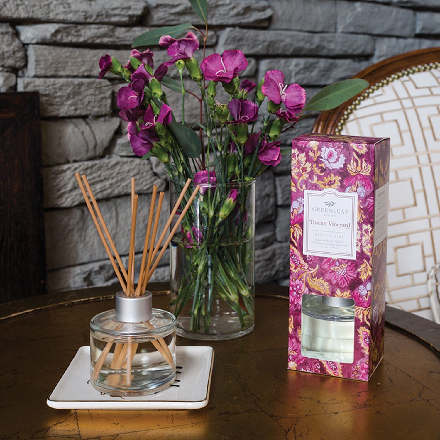Aromatischer Reed Diffuser neben einer Vase mit lila Blumen und der Produktverpackung.