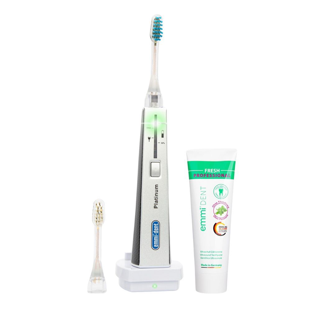 Ultraschallzahnbürste Platinum Carbon, Ladestation, Ersatzbürste und Zahnpasta. Zahnbürste mit grünem Licht. Zahnpasta mit "emmi-dent"-Logo.