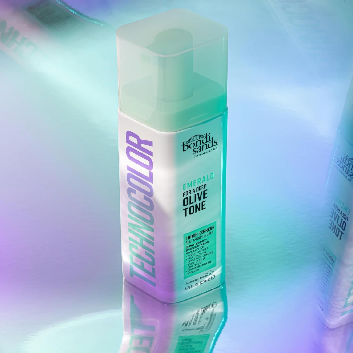 Bondi Sands Selbstbräunungsschaum, Emerald, für einen tiefen Olivton. Flasche mit Sprühkopf, auf schimmerndem Hintergrund.