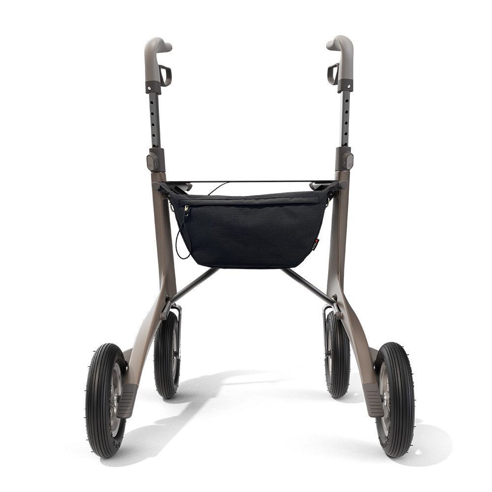 Rollator mit schwarzer Tasche. Vier Räder. Graue Rahmenkonstruktion. Kleines rotes Logo.