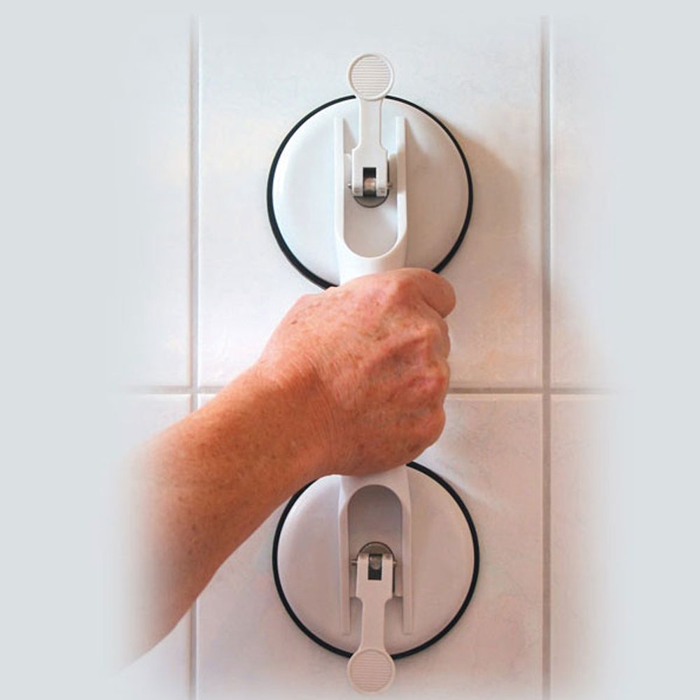 Weißer Saughaltegriff mit zwei Saugnäpfen und Hebeln, der von einer Hand an einer gefliesten Wand gehalten wird.