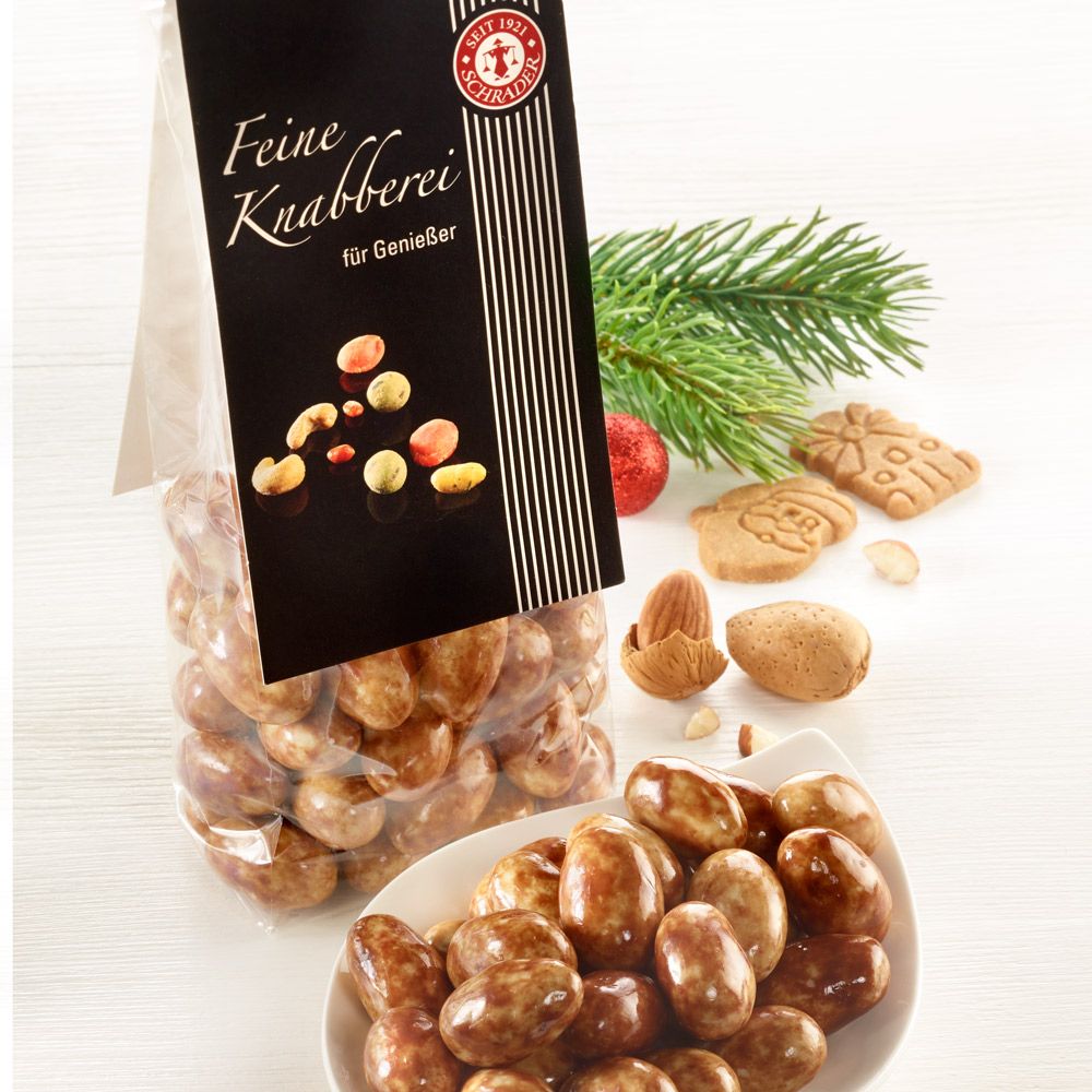 Schrader Spekulatius-Mandeln in Tüte und Schale. Schwarzes Etikett mit "Feine Knabberei". Mandeln, Gebäck und Tannenzweig.