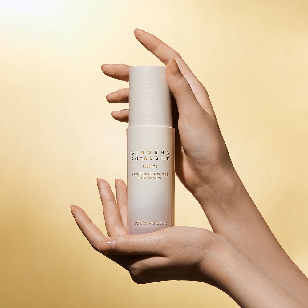 Hände halten eine beige Flasche mit Schriftzug GINSENG ROYAL SILK ESSENCE. Untertitel: Brightening & Wrinkle Improvement. Marke: NATURE REPUBLIC.