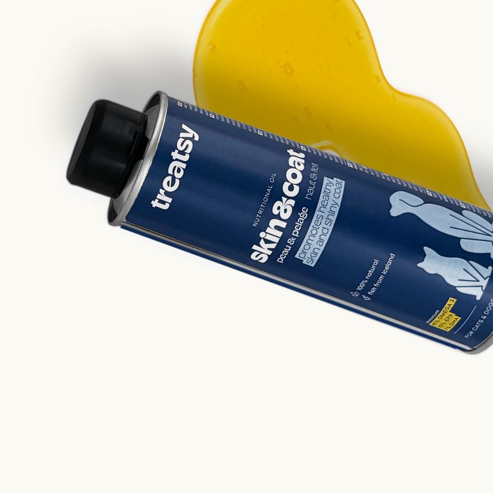 Blaue Dose mit schwarzem Deckel, Treatsy Skin & Coat, liegt schräg. Gelbes Öl daneben. Für Hunde und Katzen.
