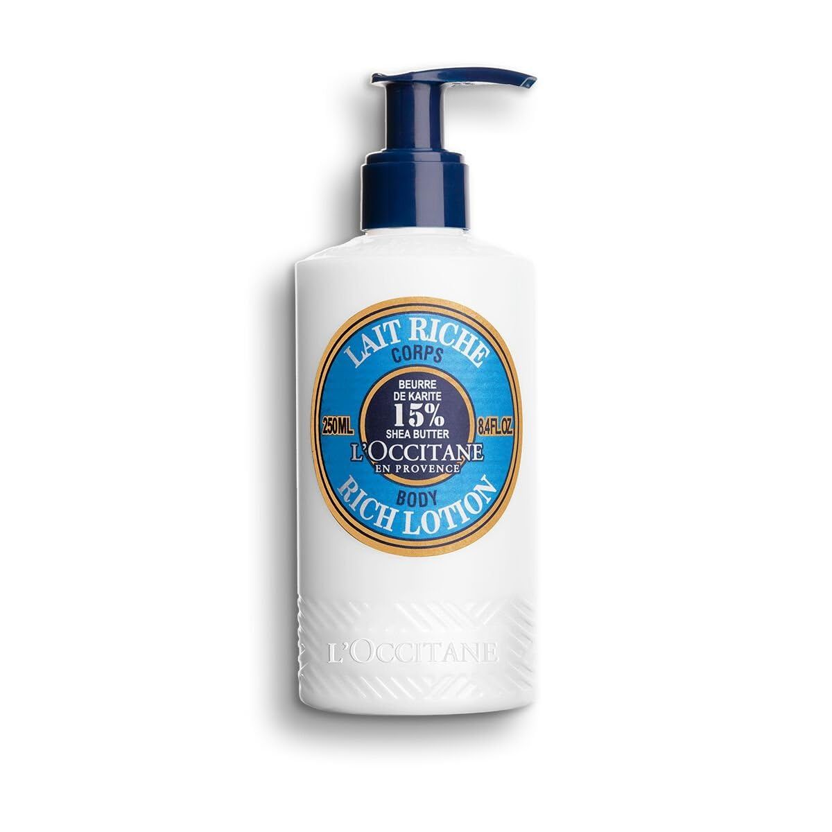 Weiße Flasche mit blauem Pumpkopf. Aufschrift: Lait Riche Corps, 15% Shea Butter, L'Occitane, Body Rich Lotion.