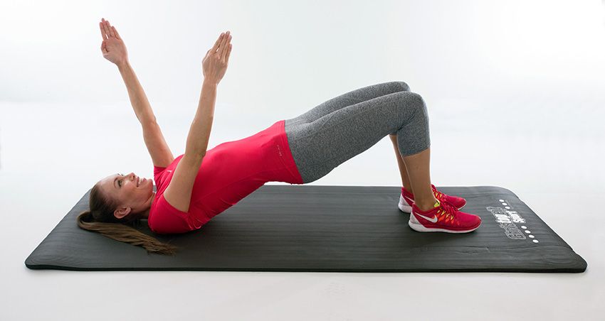 Person auf Fitnessmatte, Brücke haltend. Matte mit weißem Logo. Person trägt Sportkleidung.