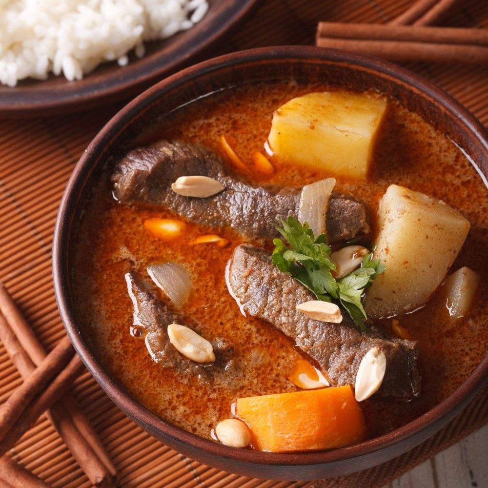 Nahaufnahme von Massaman Curry in einer Schüssel. Enthält Fleisch, Kartoffeln, Erdnüsse und Gemüse. Braune Schüssel.