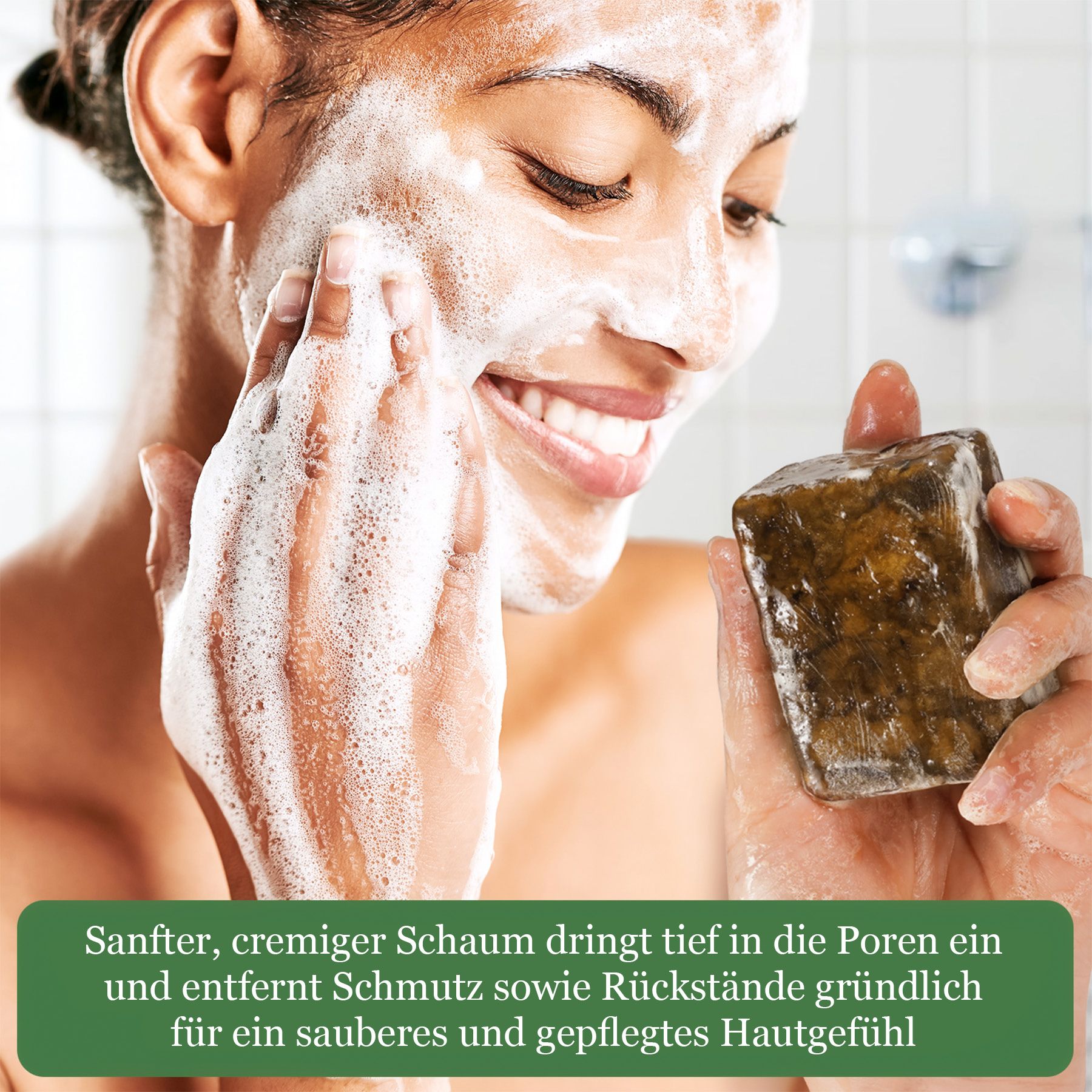 Eine Frau mit schäumendem Gesicht hält einen dunklen Seifenblock in der Hand.
