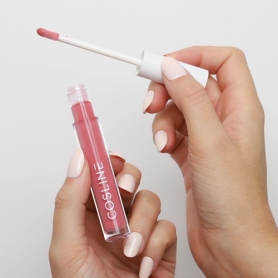 Hände halten einen Lipgloss-Flakon und Applikator. Der Flakon ist transparent mit rosa Inhalt. Der Schriftzug COSline ist sichtbar.