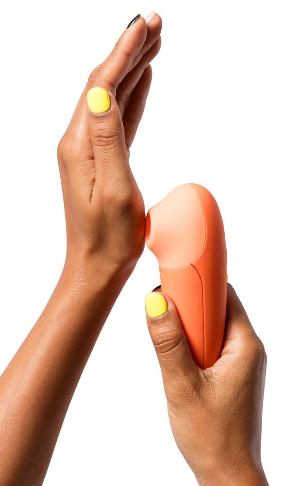 Hände halten orangefarbenes Gerät. Oberteil hellorange. Gelber Nagellack. Gerät wird an der Hand gehalten.