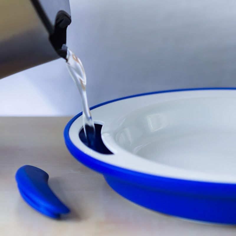 Weißer Teller mit blauem Rand. Wasser wird in eine Öffnung gegossen. Ein blaues Teil liegt daneben.