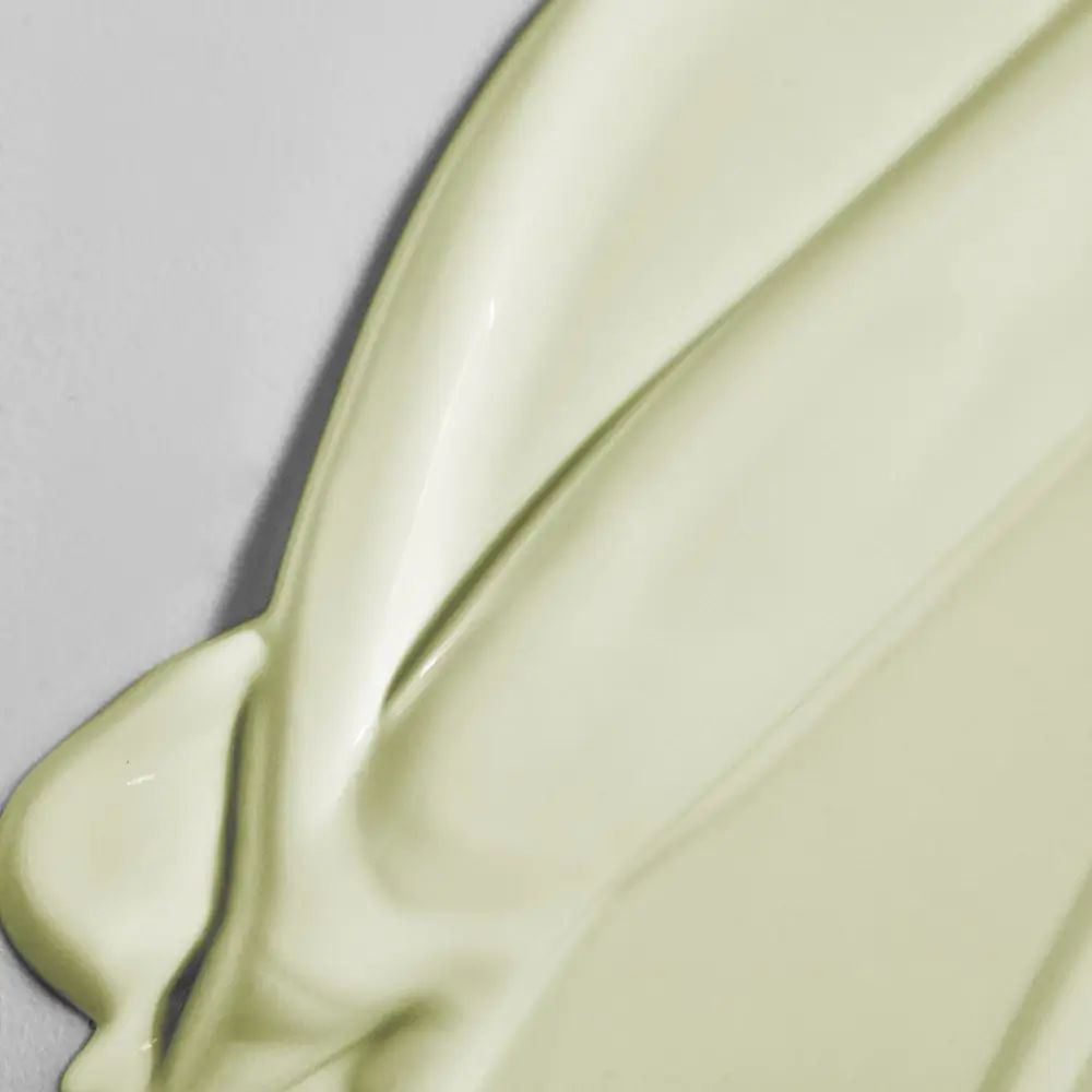 Nahaufnahme von cremiger, hellgrüner Sonnencreme. Die Textur ist glatt und glänzend. Die Creme ist auf einer hellen Oberfläche verteilt.
