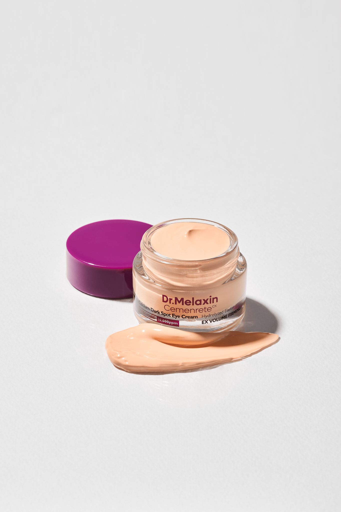 Tiegel Dr.Melaxin Cemenrete Calcium Dark Spot Eye Cream. Lila Deckel, beige Creme. Creme-Abstrich daneben.
