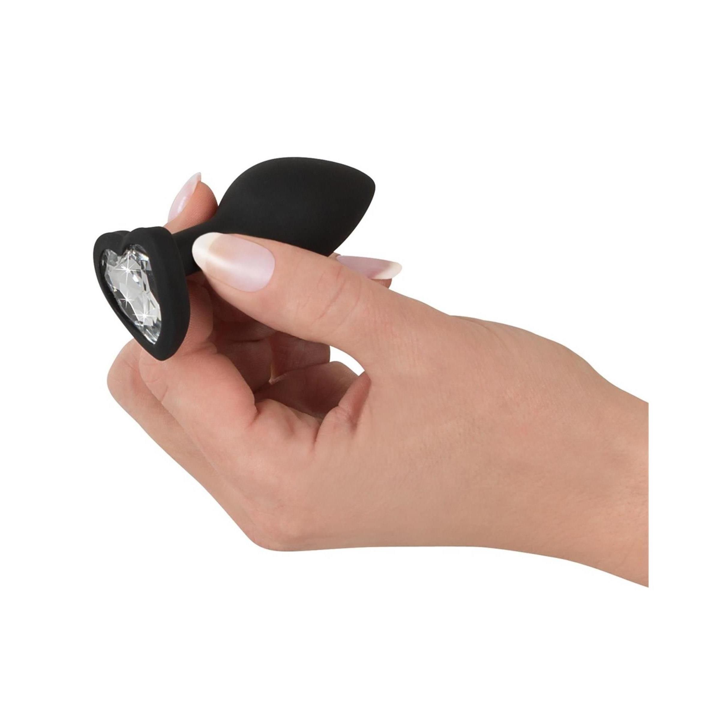 Hand hält schwarzen Silikon-Butt-Plug mit Herz-Kristall-Dekor. Herzbasis.