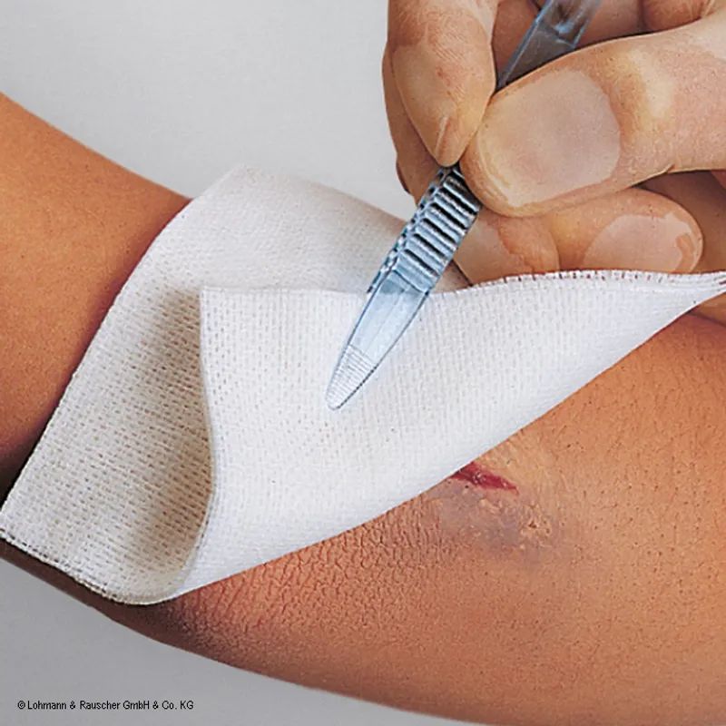 Weiße Augenlochkompresse auf Arm. Einmalige Kompresse. Logo von Lohmann & Rauscher.