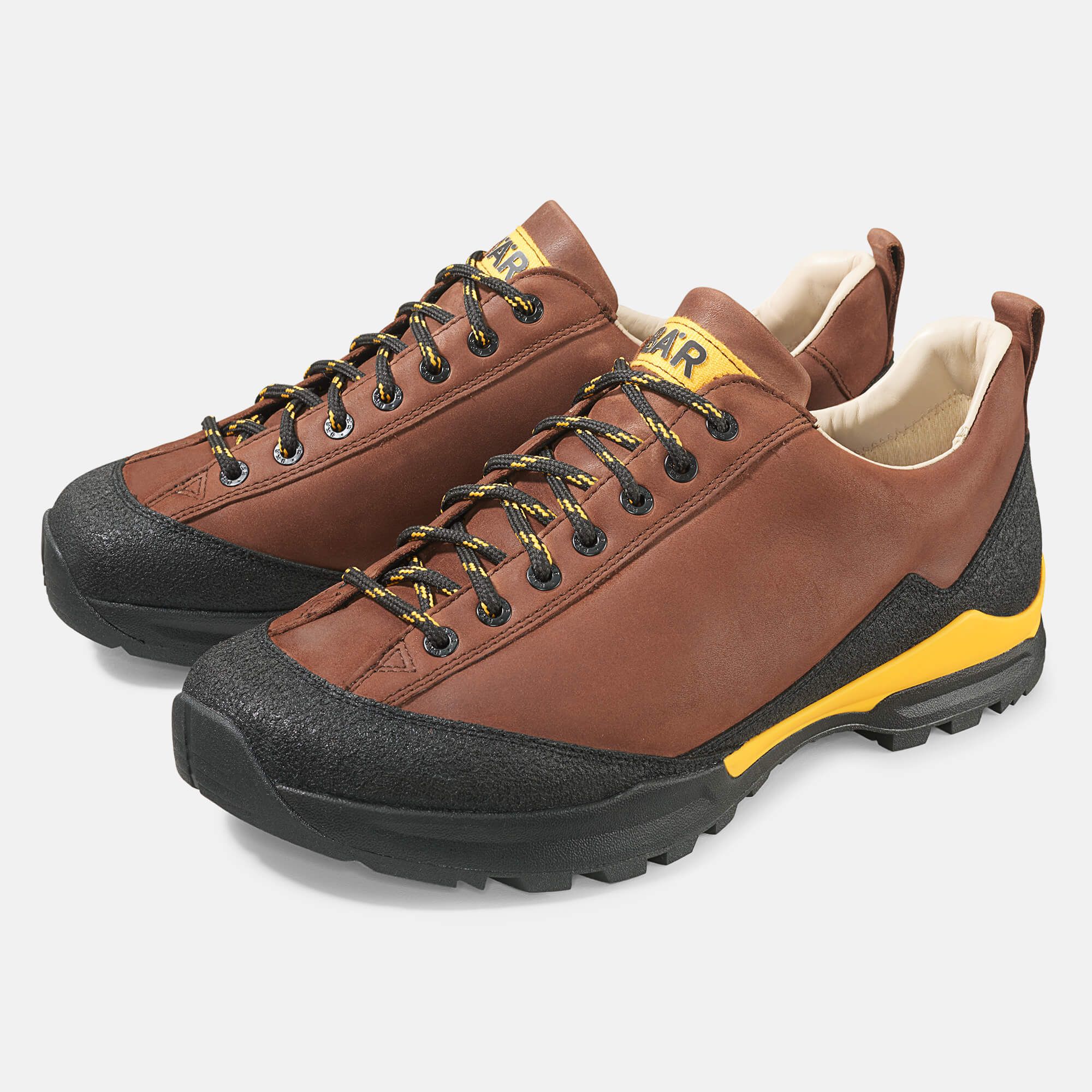 Braune Wanderschuhe mit schwarzen Sohlen und Schnürsenkeln. Gelbe Akzente und das Wort "BÄR" sind sichtbar.