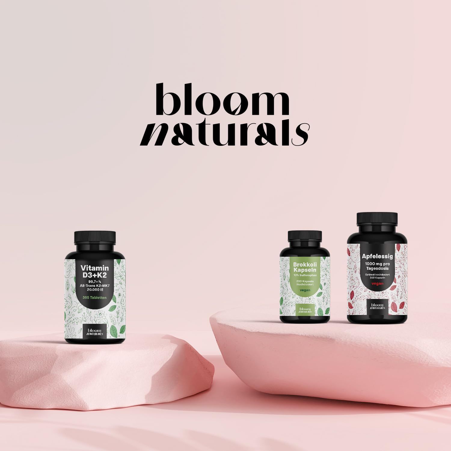 Drei Flaschen auf Podesten. Bloom Naturals. Vitamin D3+K2, Brokkoli, Apfeleisig.