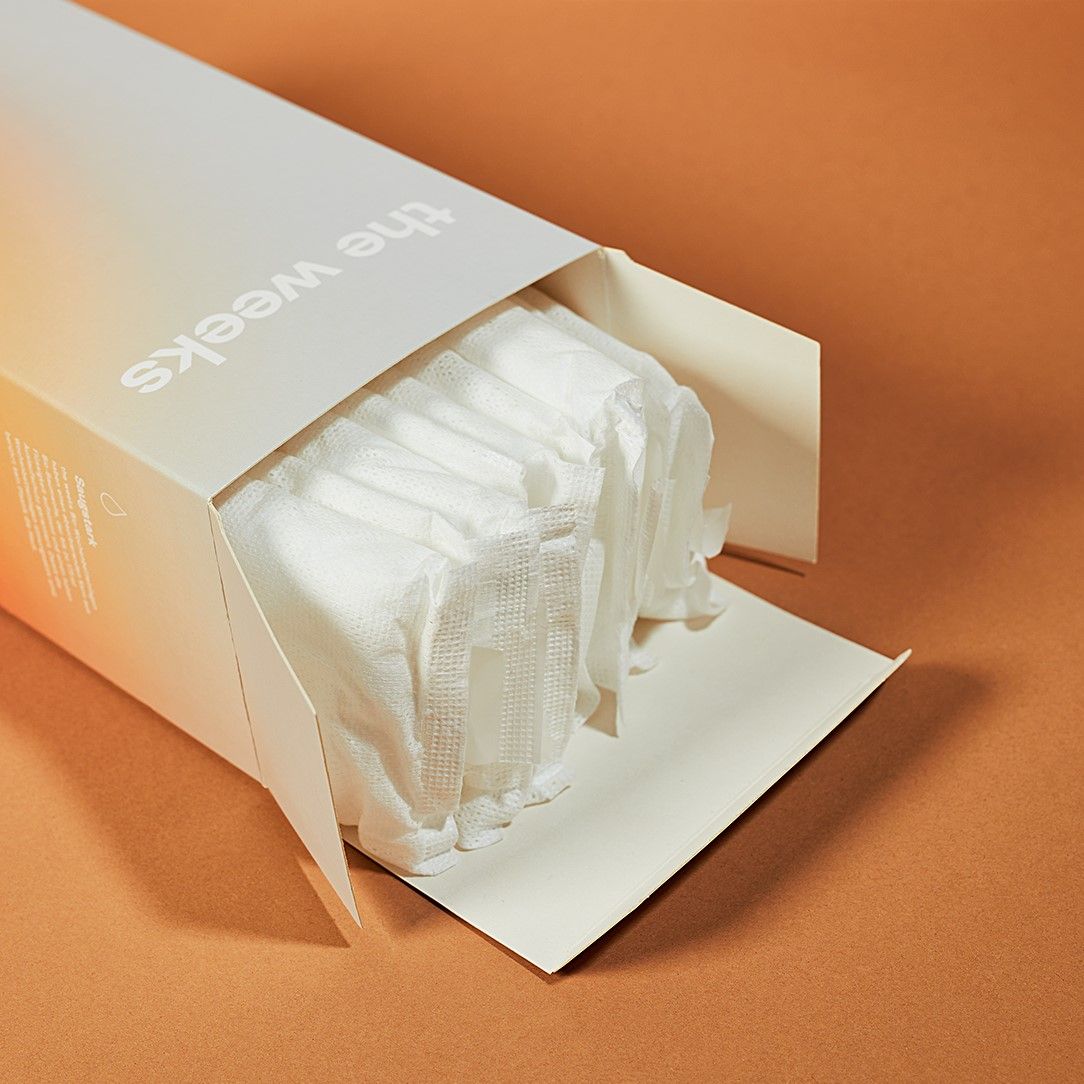 Geöffnete Produktverpackung mit weißen, gefalteten Binden. Aufdruck "the weeks".