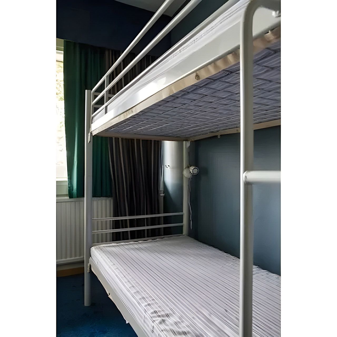 Etagenbett mit weißem Metallrahmen. Matratzen mit weiß-grauen Streifen. Blauer Hintergrund.