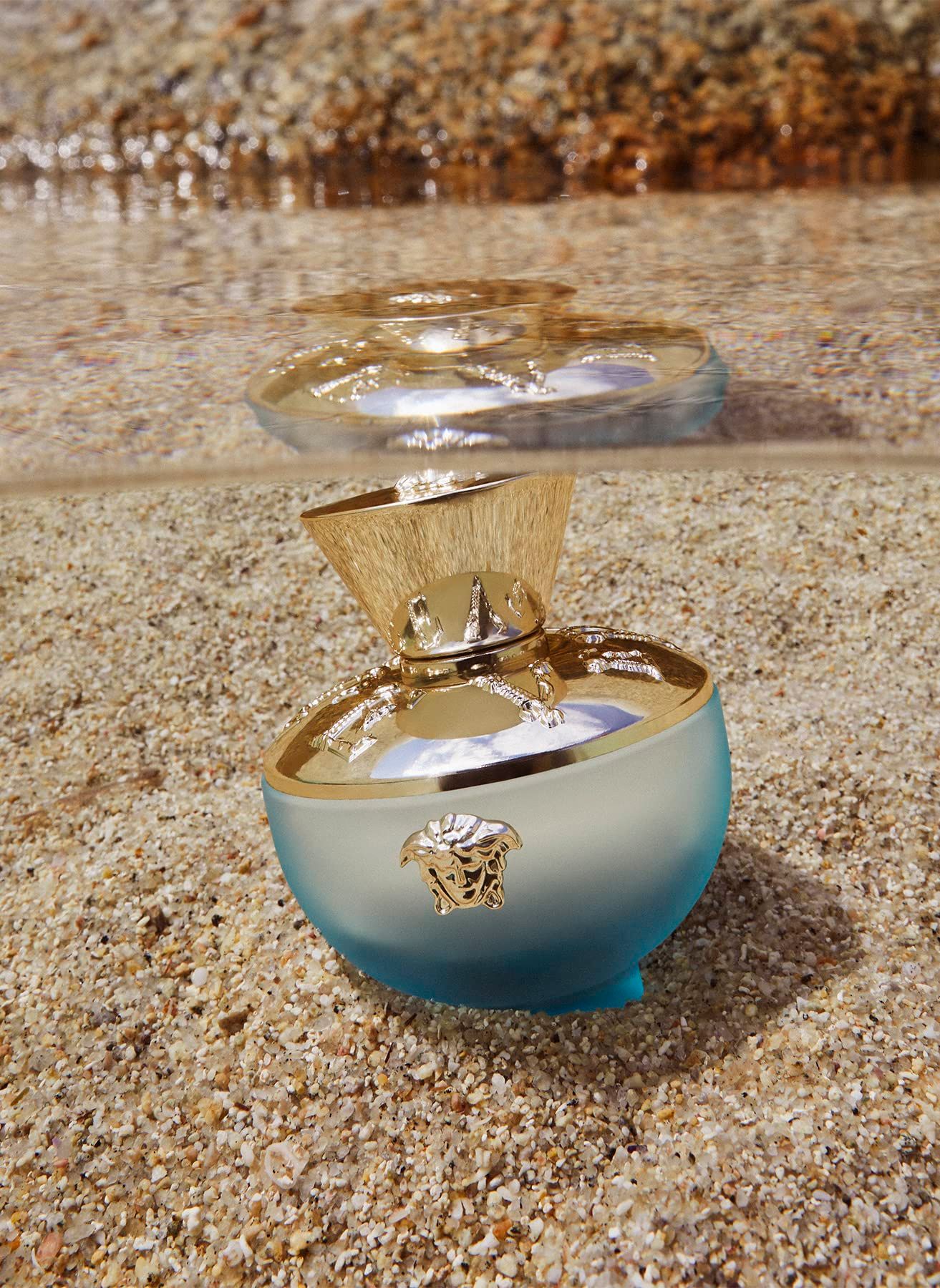 Türkisblaue Flasche mit goldenem Deckel und Logo. Flasche liegt auf Sand, Wasser im Hintergrund.