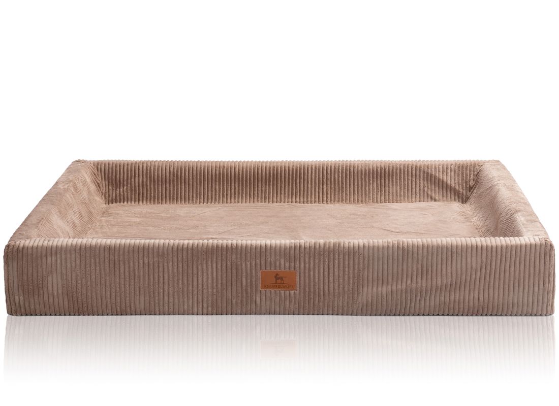 Orthopädisches Hundebett, rechteckig, beige, mit erhöhtem Rand. Cord-Optik. Kleines Logo-Etikett. Auf weißem Hintergrund.